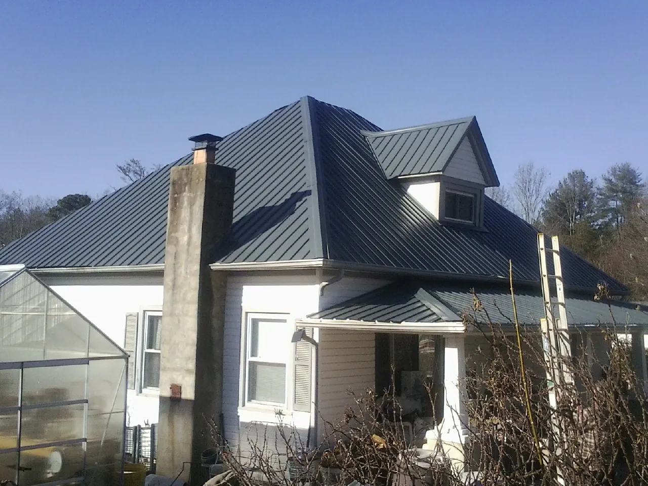 Dark blue standing seam metal roof on a white farmhouse with dormer in Pascoag