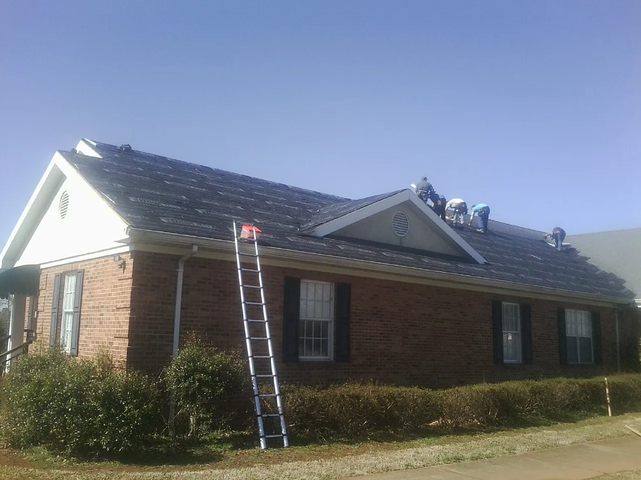 Crew tearing shingles off a brick ranch roof with a ladder set — Emergency Roof Repair work by our crew in Pascoag