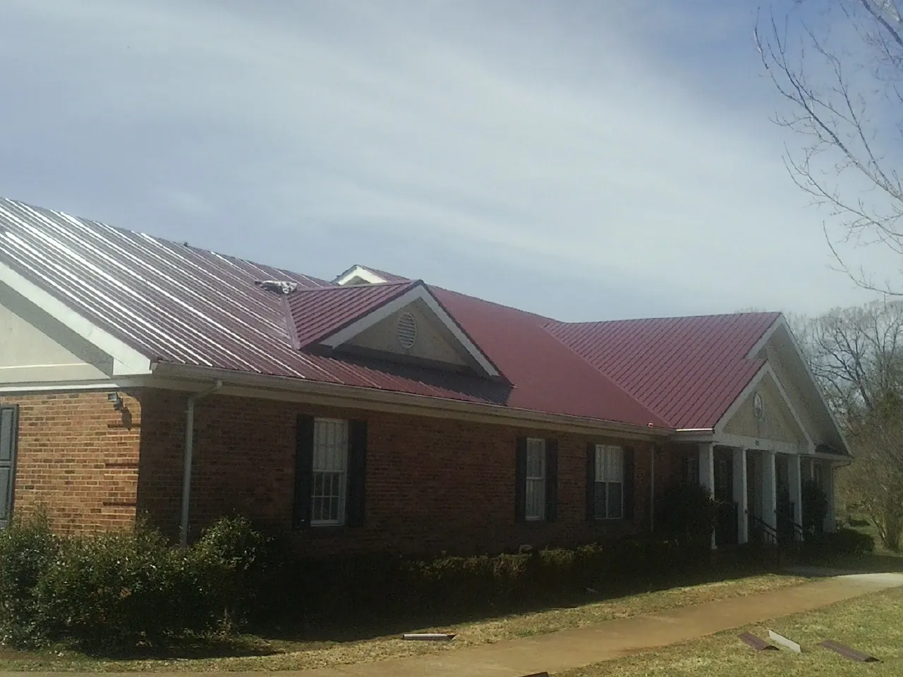 Red metal roof with gabled entries on a long brick building, from a Hail Damage Roof Repair job in Pascoag