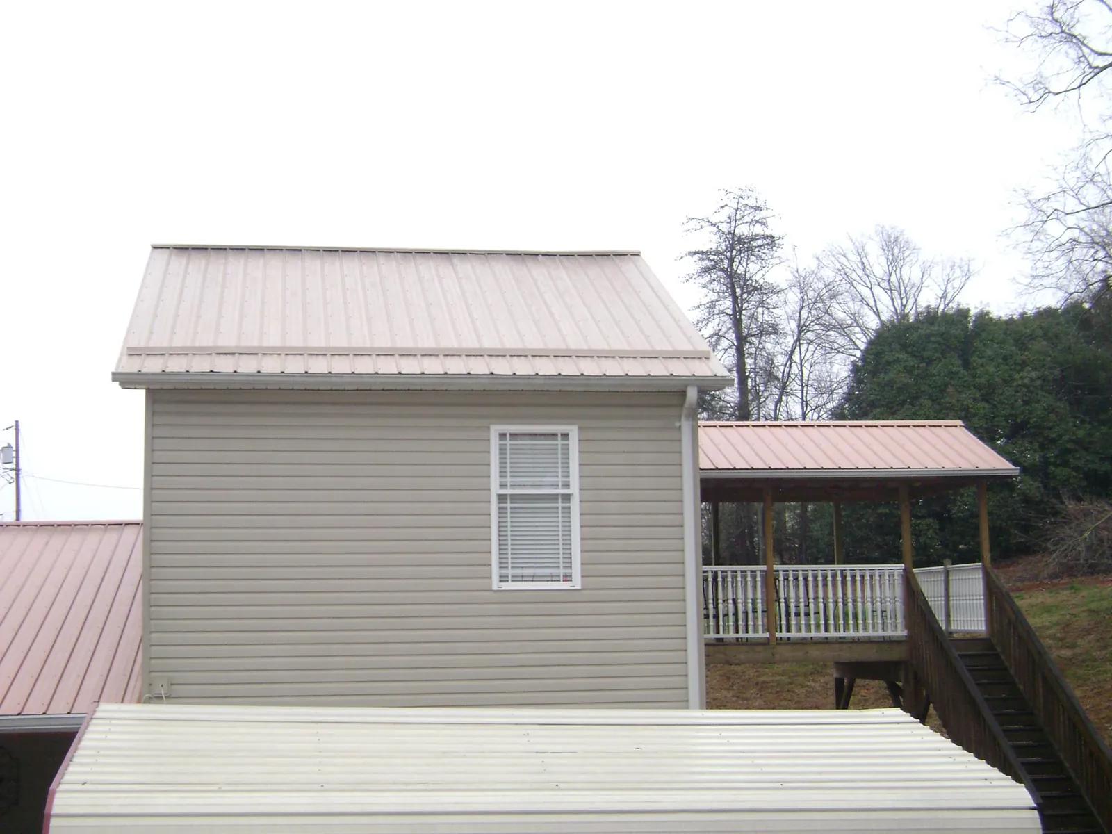 Tan metal roofs on a two story addition and attached porch, from a Roof Replacement job in Pascoag